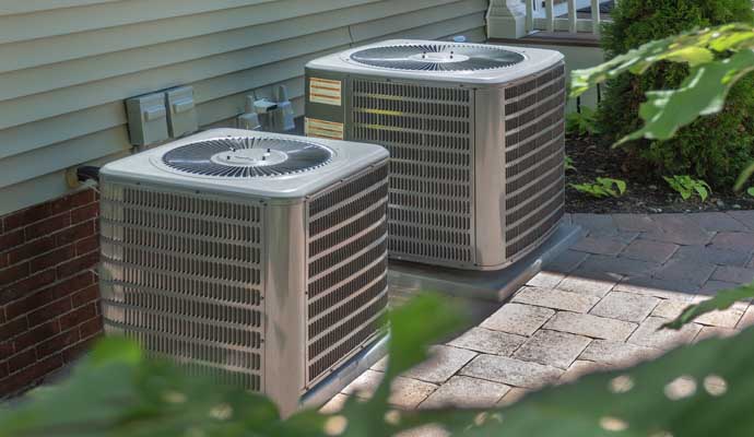 two central air conditioning units placed on a paved area