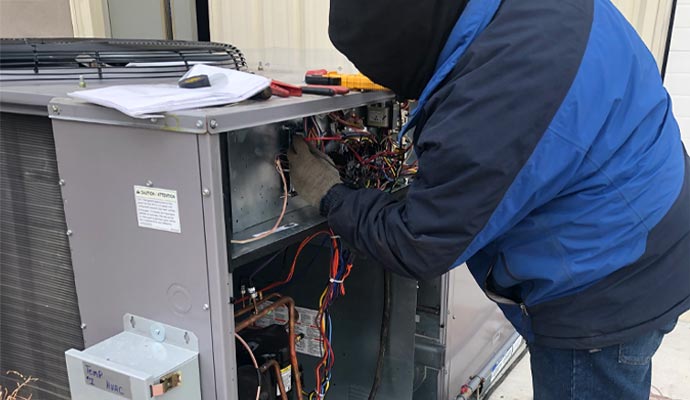 Technician repairing electrical components inside an outdoor AC unit