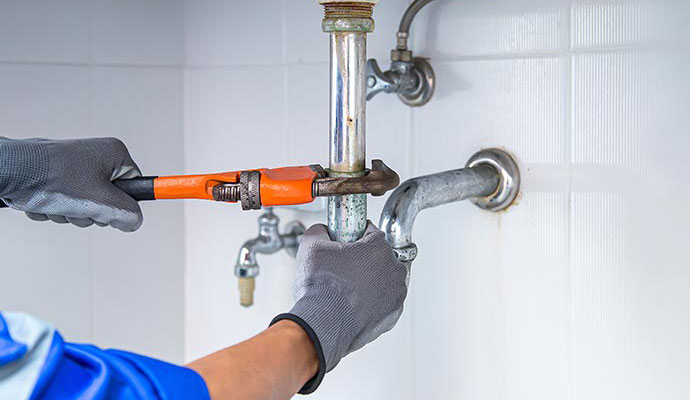 A plumber using a wrench to fix a pipe under a sink